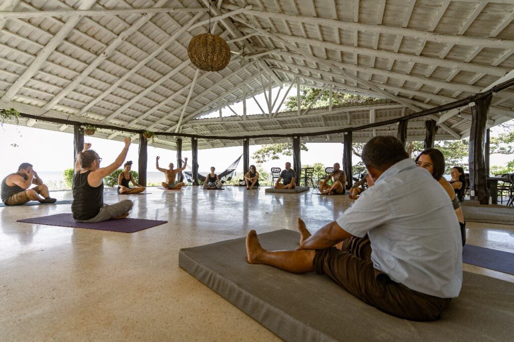 Grupo de personas participando en una sesión de yoga guiada bajo un rancho en Guanacaste, como parte de un retiro de bienestar en Costa Rica.