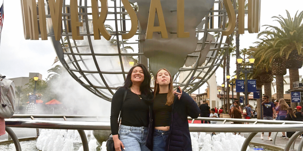 Madre migrante nicaragüense junto a su hija posando frente al icónico globo de Universal Studios, símbolo de unión familiar en el extranjero.