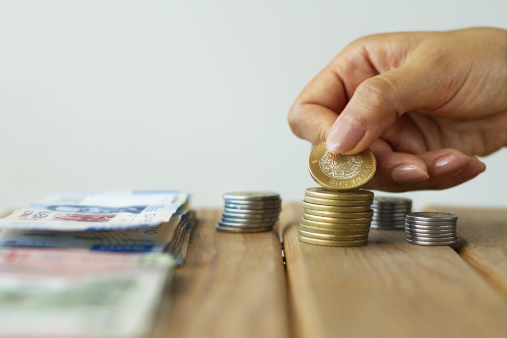 Mano apilando monedas junto a billetes guatemaltecos sobre una mesa de madera, simbolizando ahorro y acceso al crédito.
