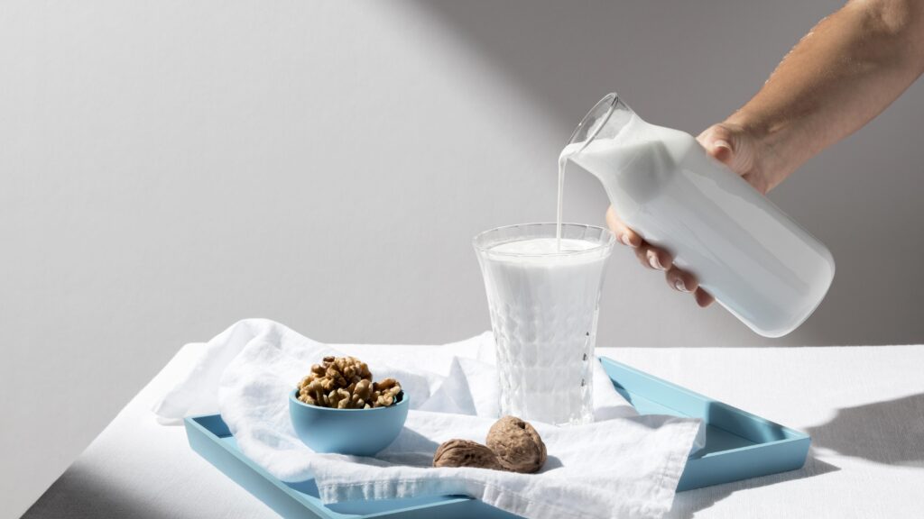Vaso de leche UHT servido con nueces sobre una bandeja azul, ideal para una alimentación saludable y sostenible.