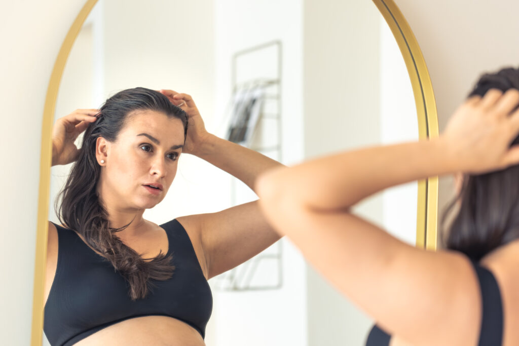Mujer joven mirándose al espejo con expresión reflexiva, representando la gestión emocional y la baja autoestima