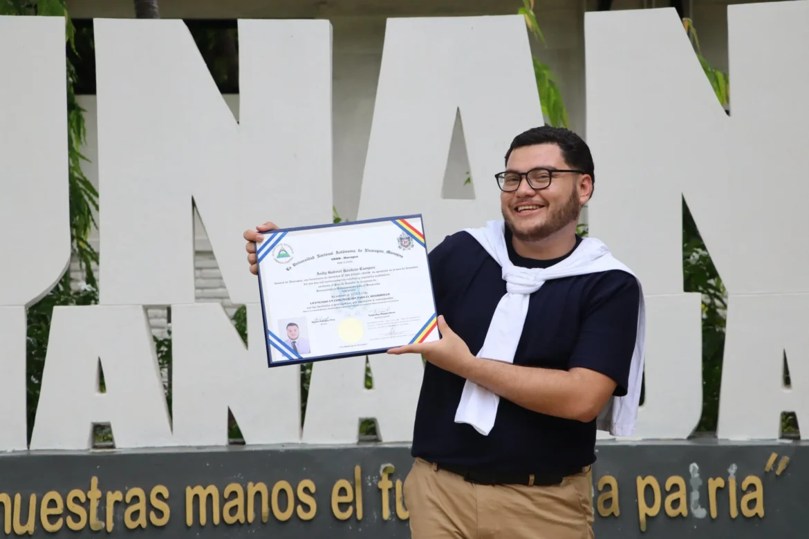 ANDY_ROSTRÁN_CANTANTE_CRISTIANO_EN_NICARAGUA.webp Andy Rostrán cantante cristiano en Nicaragua sostiene su diploma de comunicación frente a las letras de la UNAN Managua