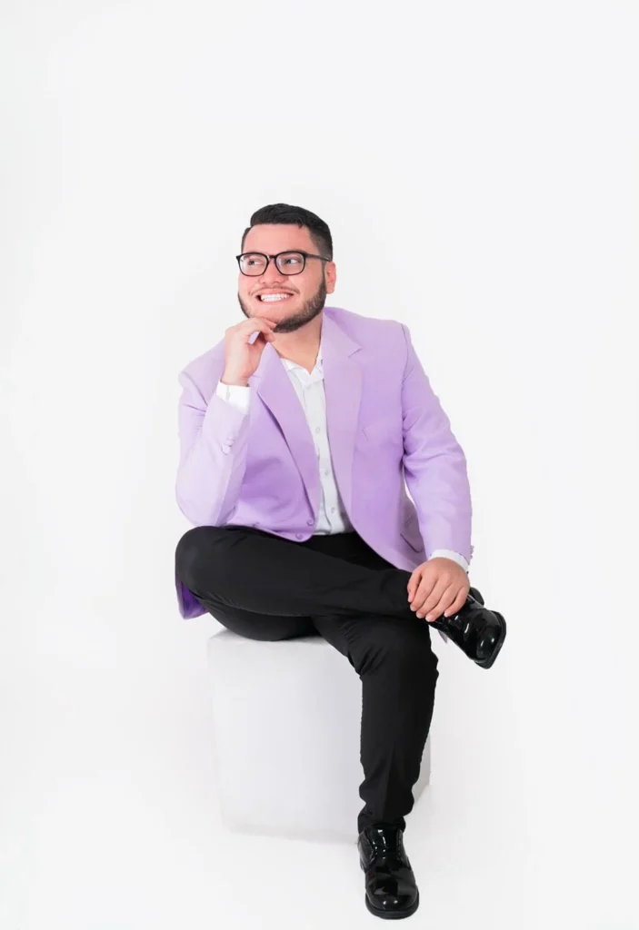 Andy Rostrán cantante cristiano en Nicaragua con saco lila sentado en estudio de fotografía con fondo blanco