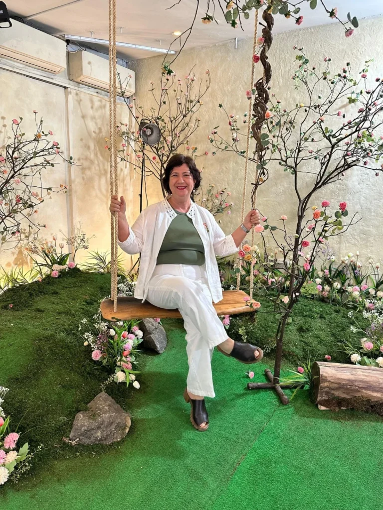 Madre nicaragüense sonriendo mientras posa en un columpio decorativo rodeado de flores y elementos naturales en un jardín interior.